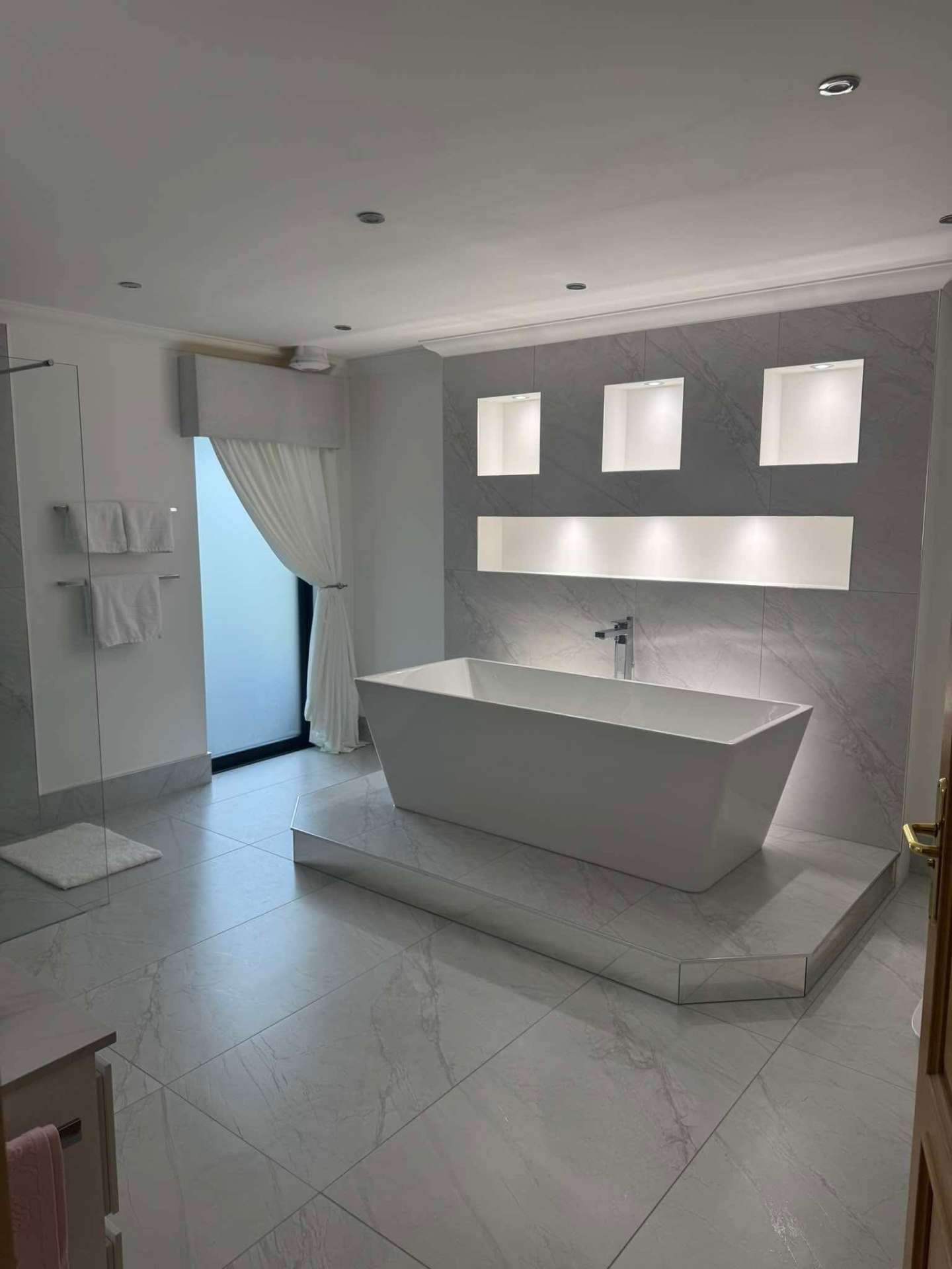Freestanding bath on a tiled plinth with lit alcoves