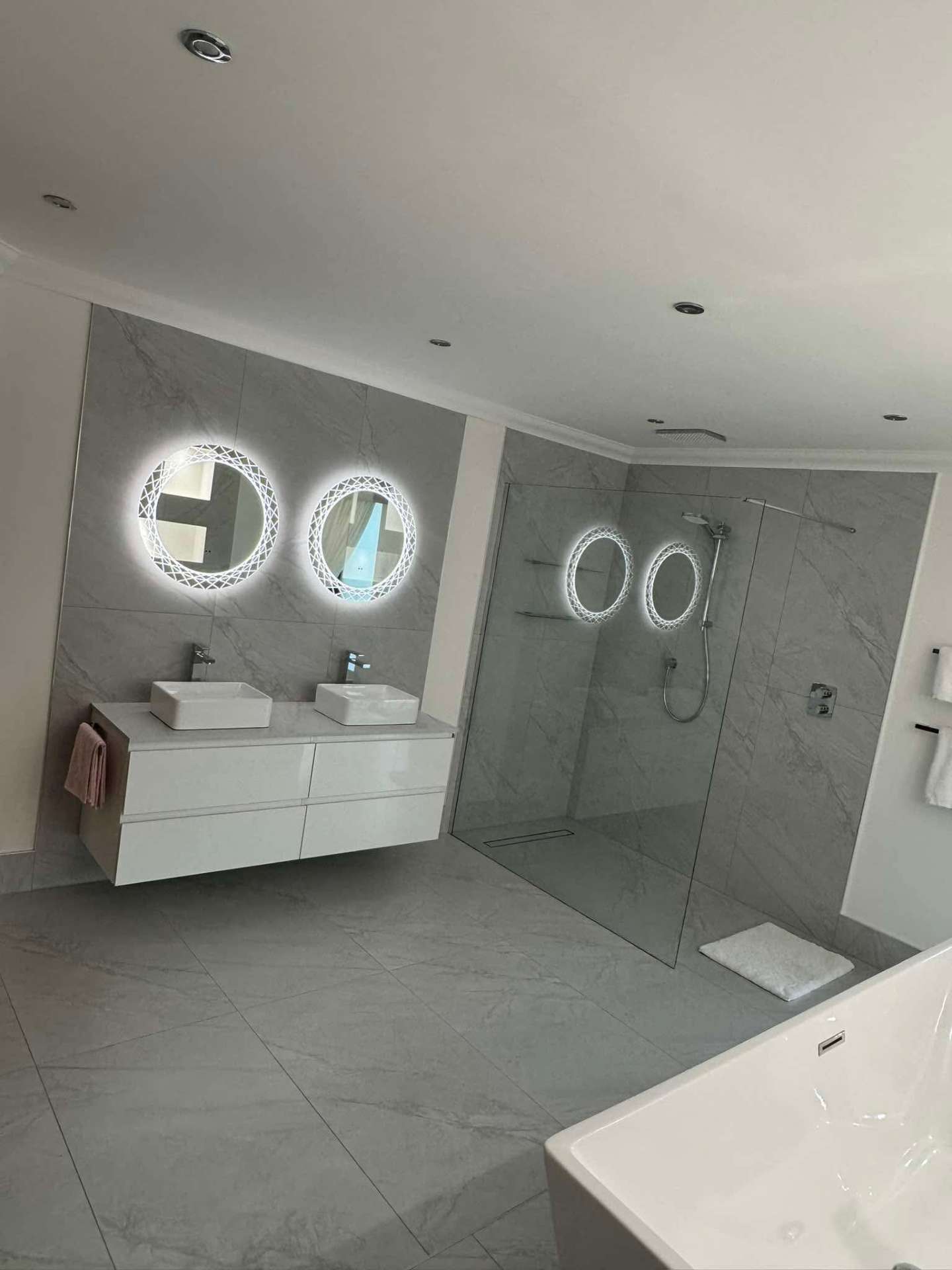 Large marble-tiled bathroom with twin LED mirrors and walk-in shower