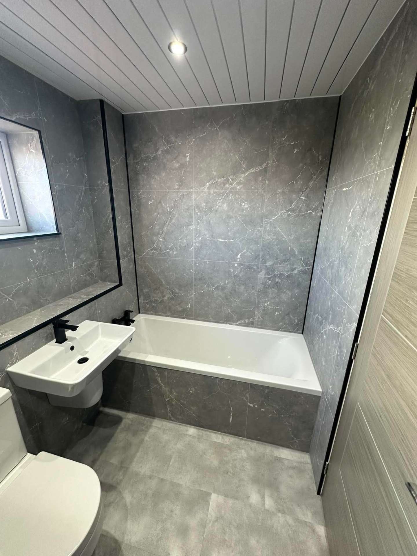 Grey marble-effect bathroom with panelled bath and black framed mirror